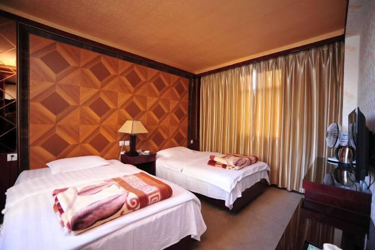 Ein Hotelzimmer mit zwei Betten, einem Nachttisch, einer Lampe, einem Spiegel und einem Fenster mit Vorhängen.