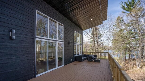 A modern house with a wooden deck, large windows, and a view of trees and a lake. - Escape to Chub Lake Retreat: Waterfront Luxury House in Carlton, Minnesota (Carlton)
