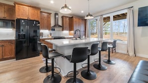 A modern kitchen with wooden cabinets, a black refrigerator, a central island with bar stools, pendant lighting, and a view of the outdoors. - Escape to Chub Lake Retreat: Waterfront Luxury House in Carlton, Minnesota (Carlton)