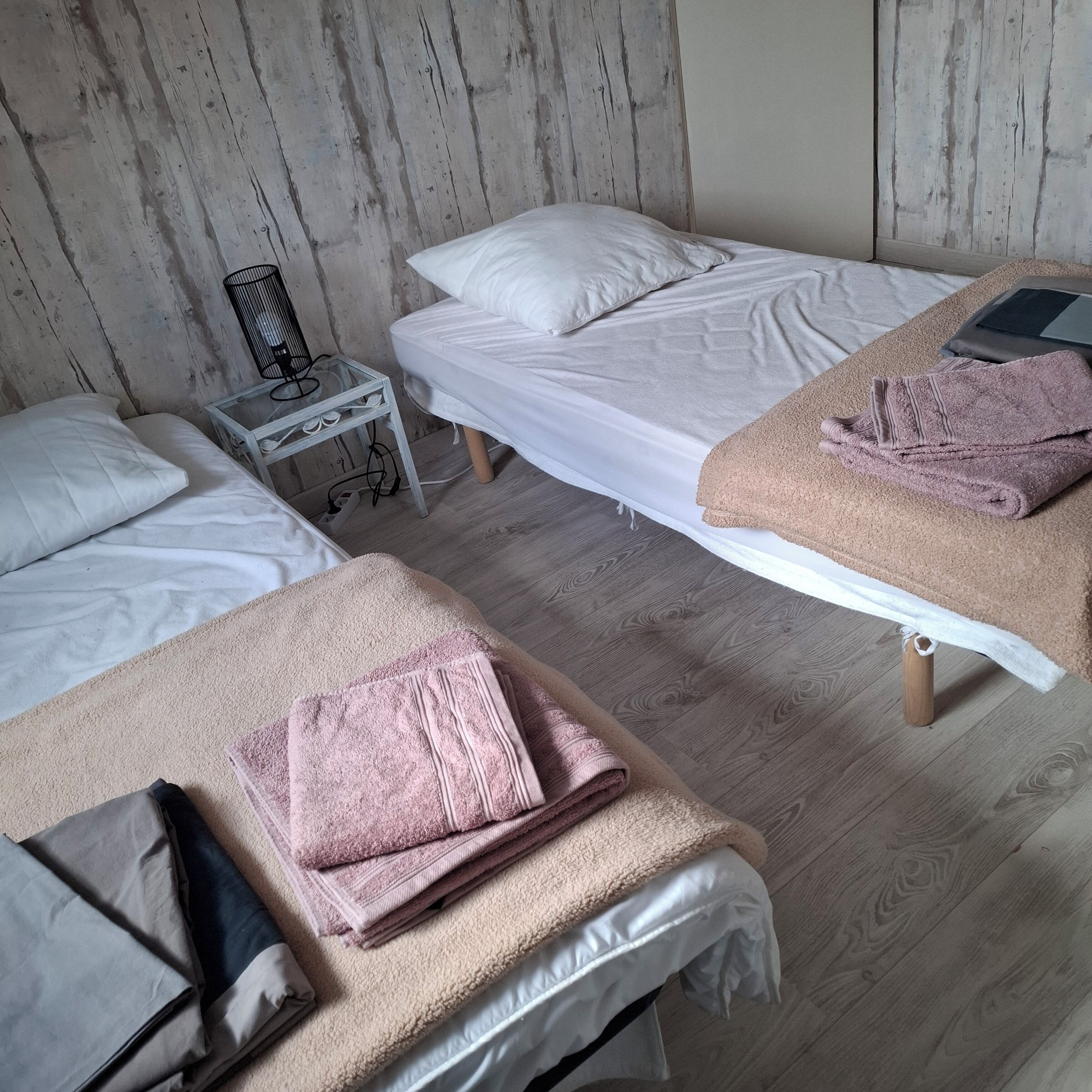 A room with two beds, a small table with a chair, and a smartphone on the right bed.