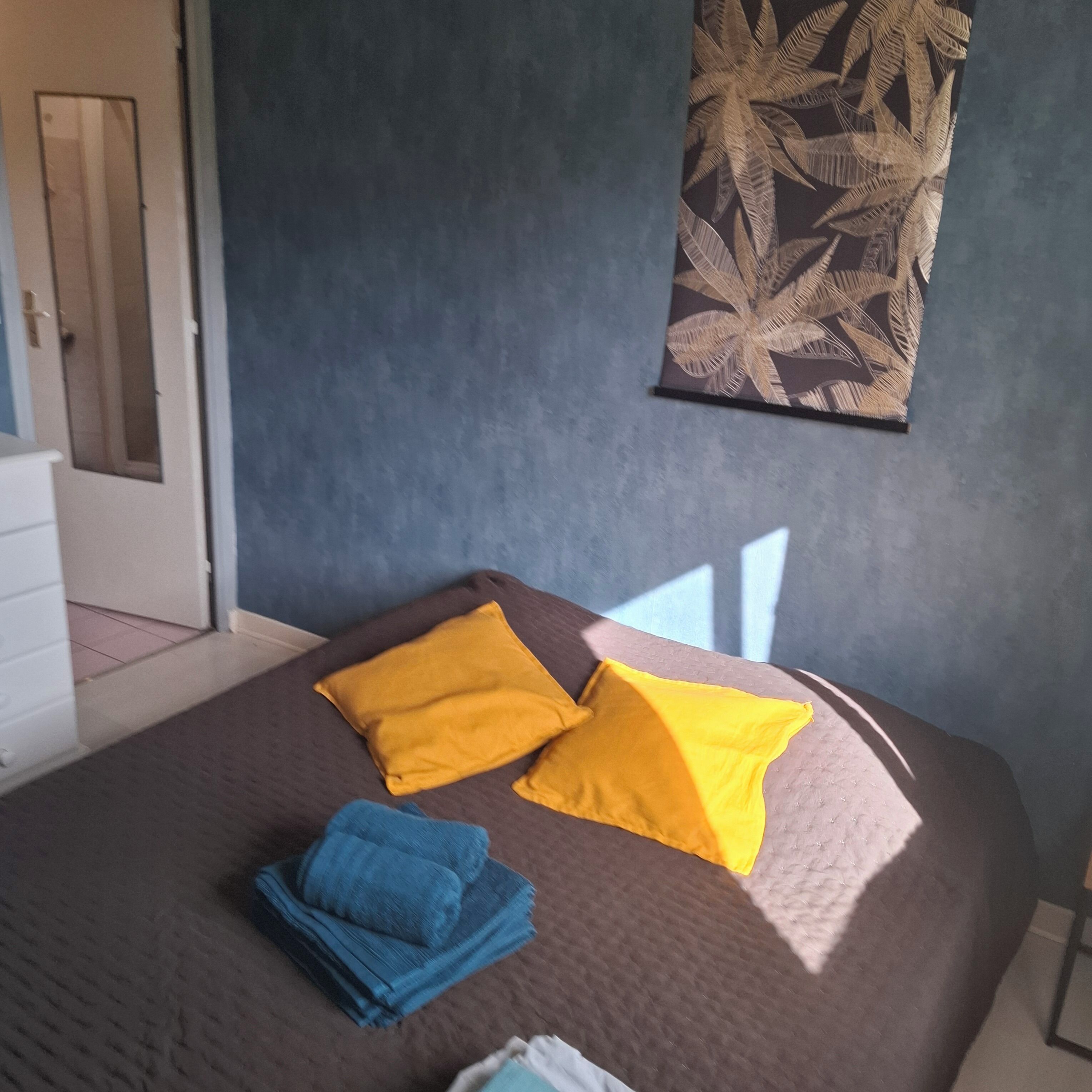 A bedroom with a bed, pillows, a folded towel, and a wall with a leaf pattern.