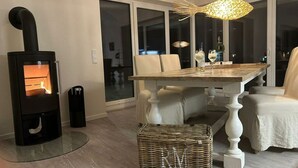 Un salón moderno con una estufa de leña, una mesa de comedor con sillas y una cesta de mimbre en el suelo.