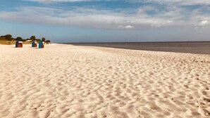 Una playa arenosa con tres cabañas azules a lo lejos.