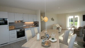 Una cocina moderna con armarios blancos, una mesa de comedor con velas y vistas al exterior a través de grandes ventanales.