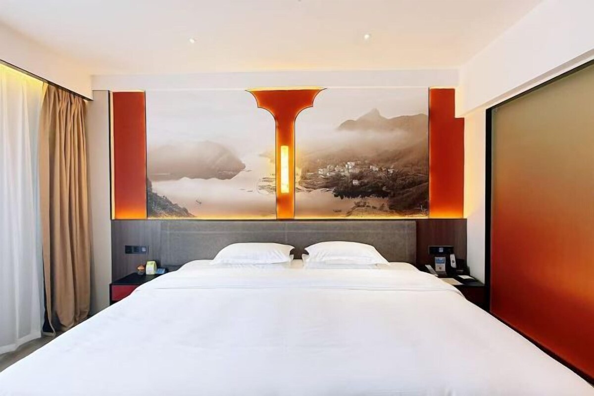 A hotel room with a large bed, a nightstand, and a wall-mounted artwork.