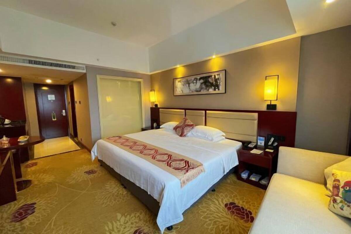 A hotel room with a large bed, bedside tables, a chair, and a door leading to another room.