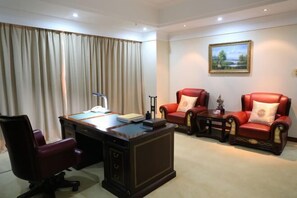 A room with a desk, two red leather chairs, a small table, and a painting on the wall.