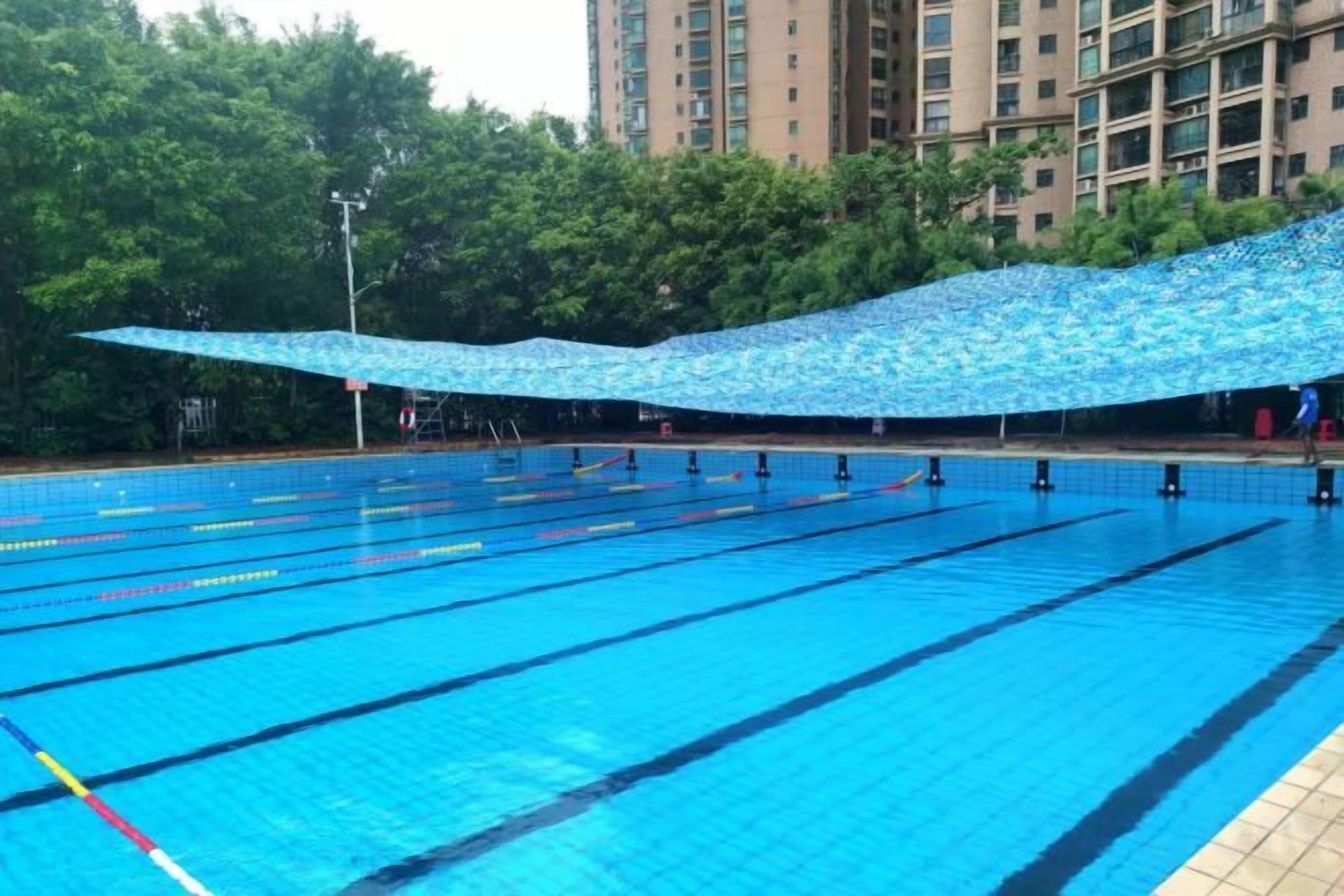 A swimming pool with multiple lanes, surrounded by trees and a building in the background.