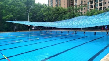 A swimming pool with multiple lanes, surrounded by trees and a building in the background.
