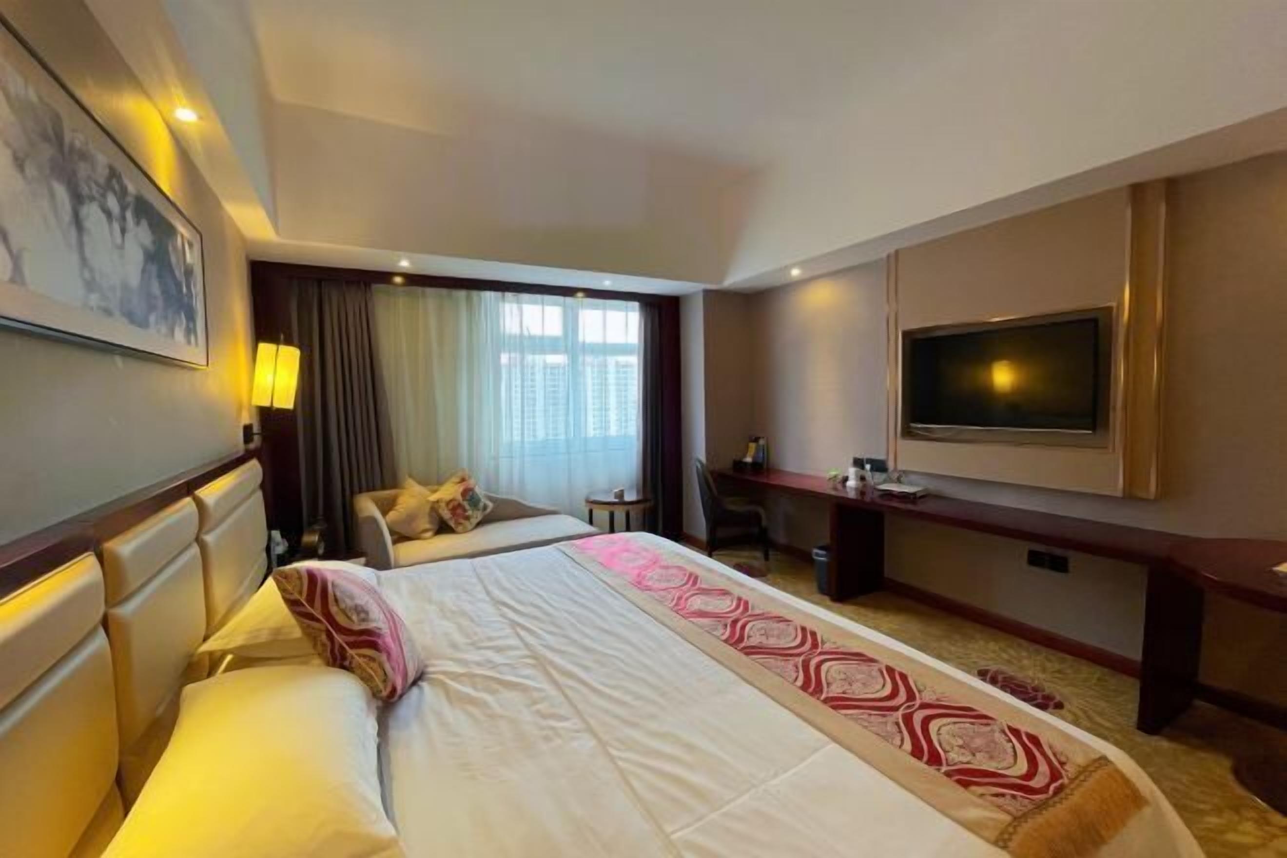 Een hotelkamer met een groot bed, een bureau, een televisie en een raam met gordijnen.