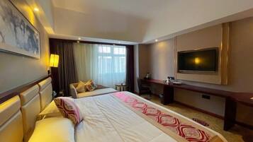 Een hotelkamer met een groot bed, een bureau, een televisie en een raam met gordijnen.