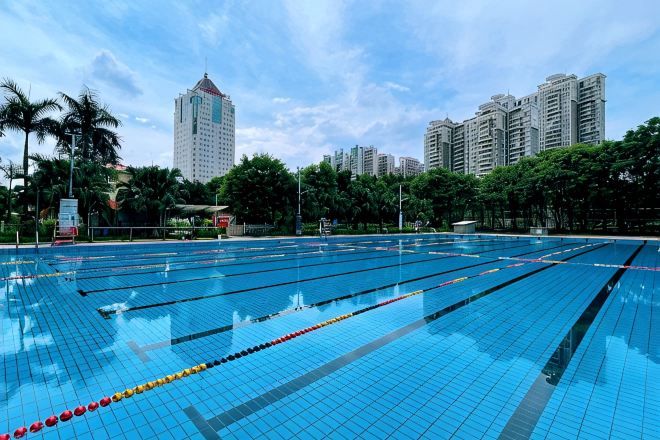A swimming pool with multiple lanes, surrounded by trees and buildings.