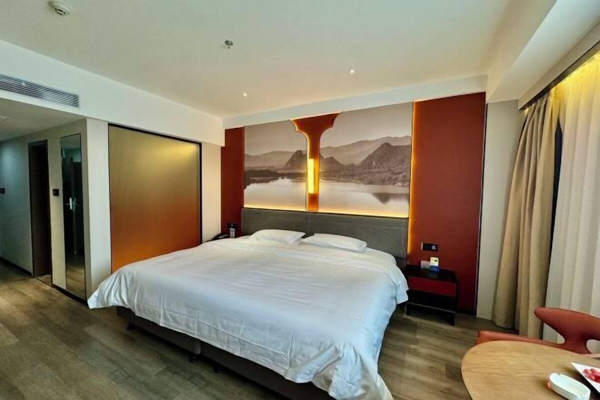 A hotel room with a large bed, a nightstand, a chair, and a view of mountains through a window.