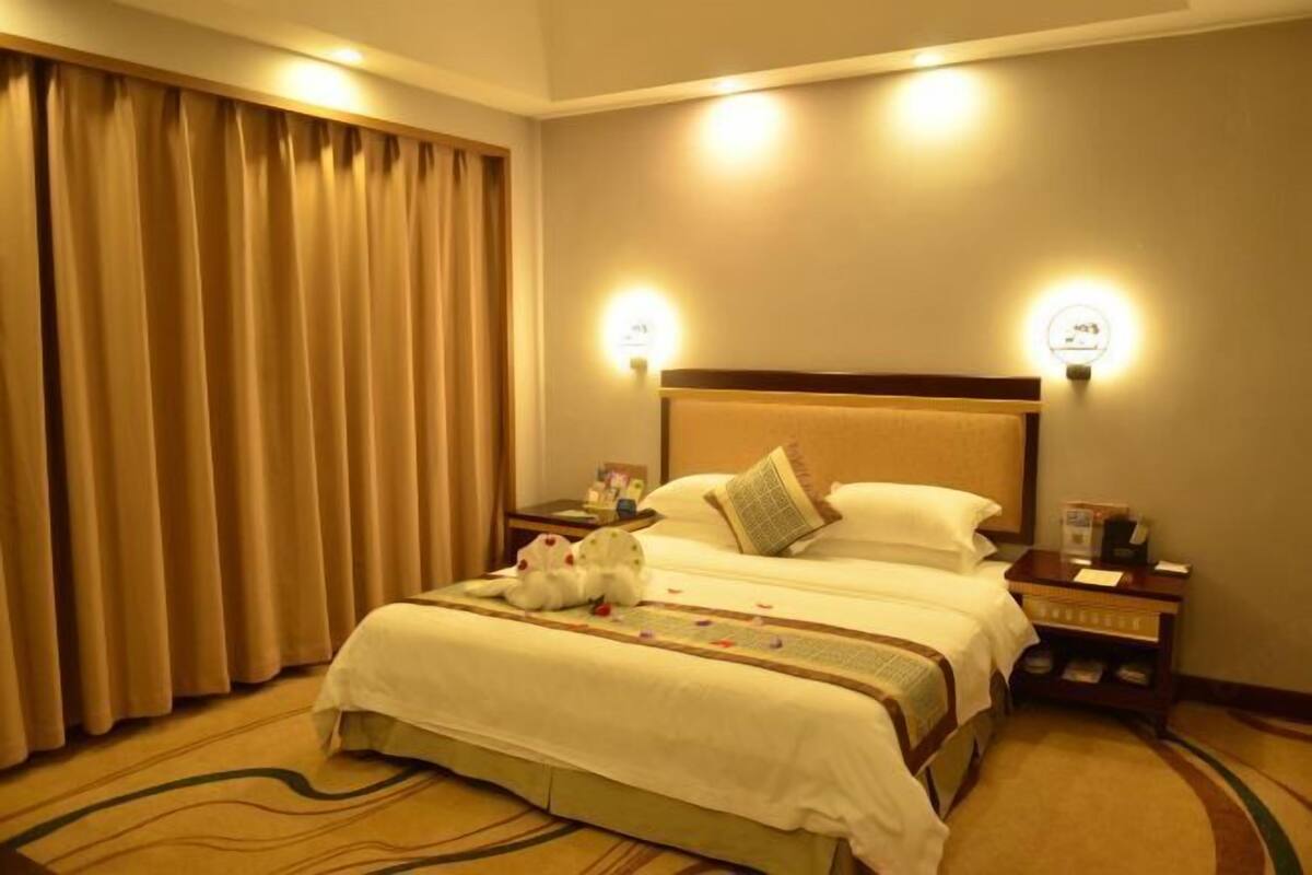 A hotel room with a large bed, two bedside tables, a nightstand, a lamp, and a curtain.