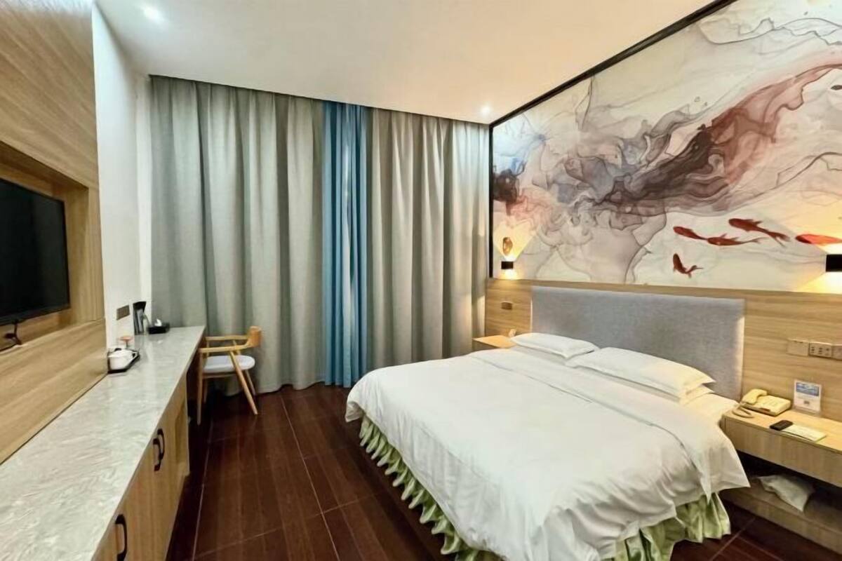 A hotel room with a bed, a desk, a chair, a TV, and a painting on the wall.