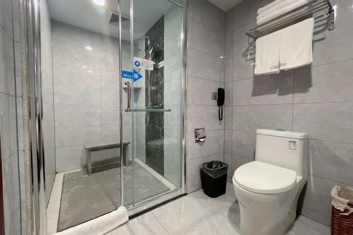 A modern bathroom with a glass-enclosed shower, a toilet, and a trash bin.