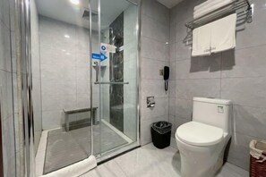 A modern bathroom with a glass-enclosed shower, a toilet, and a trash bin.