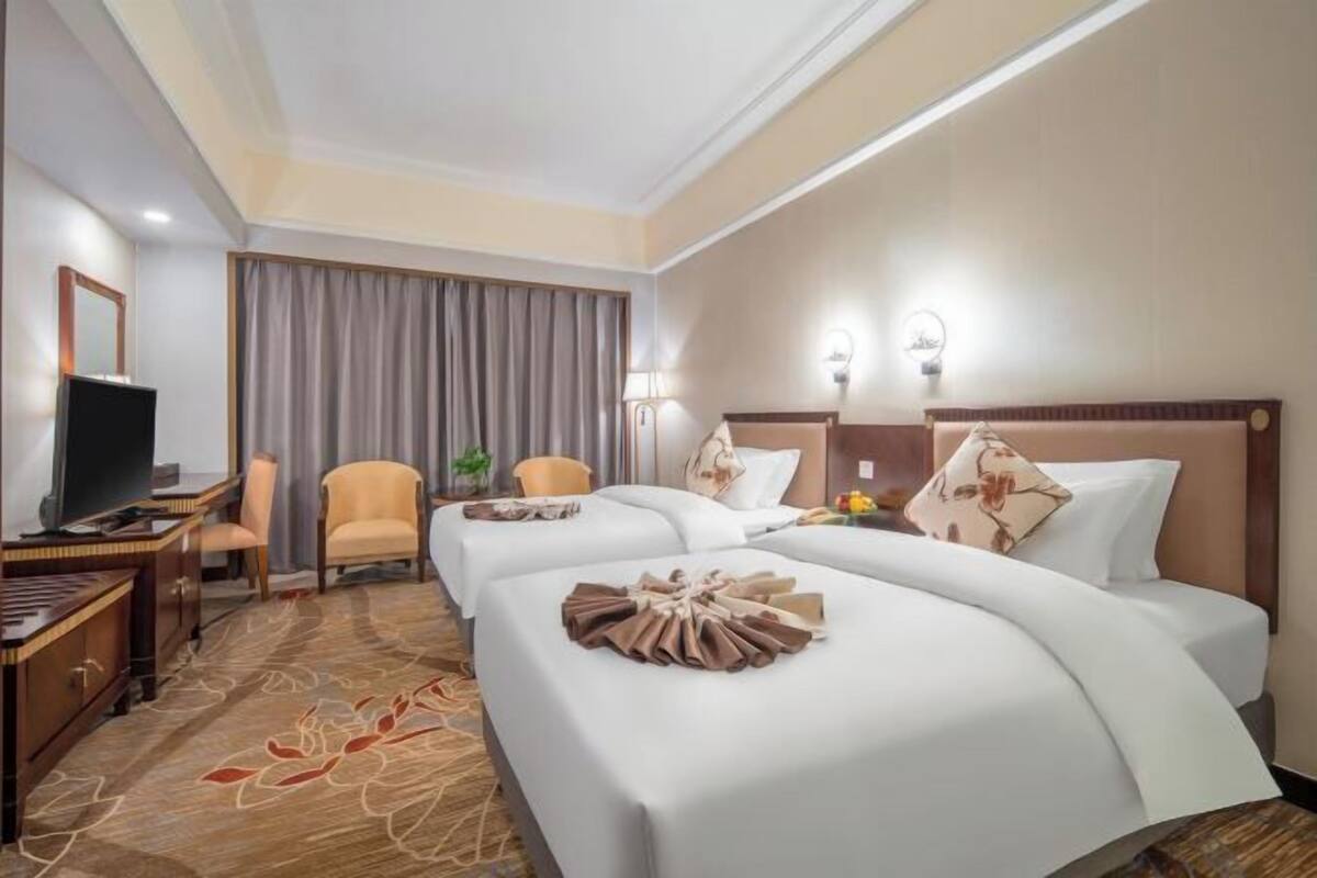 A hotel room with two beds, a desk with a TV, a chair, and a large window with curtains.