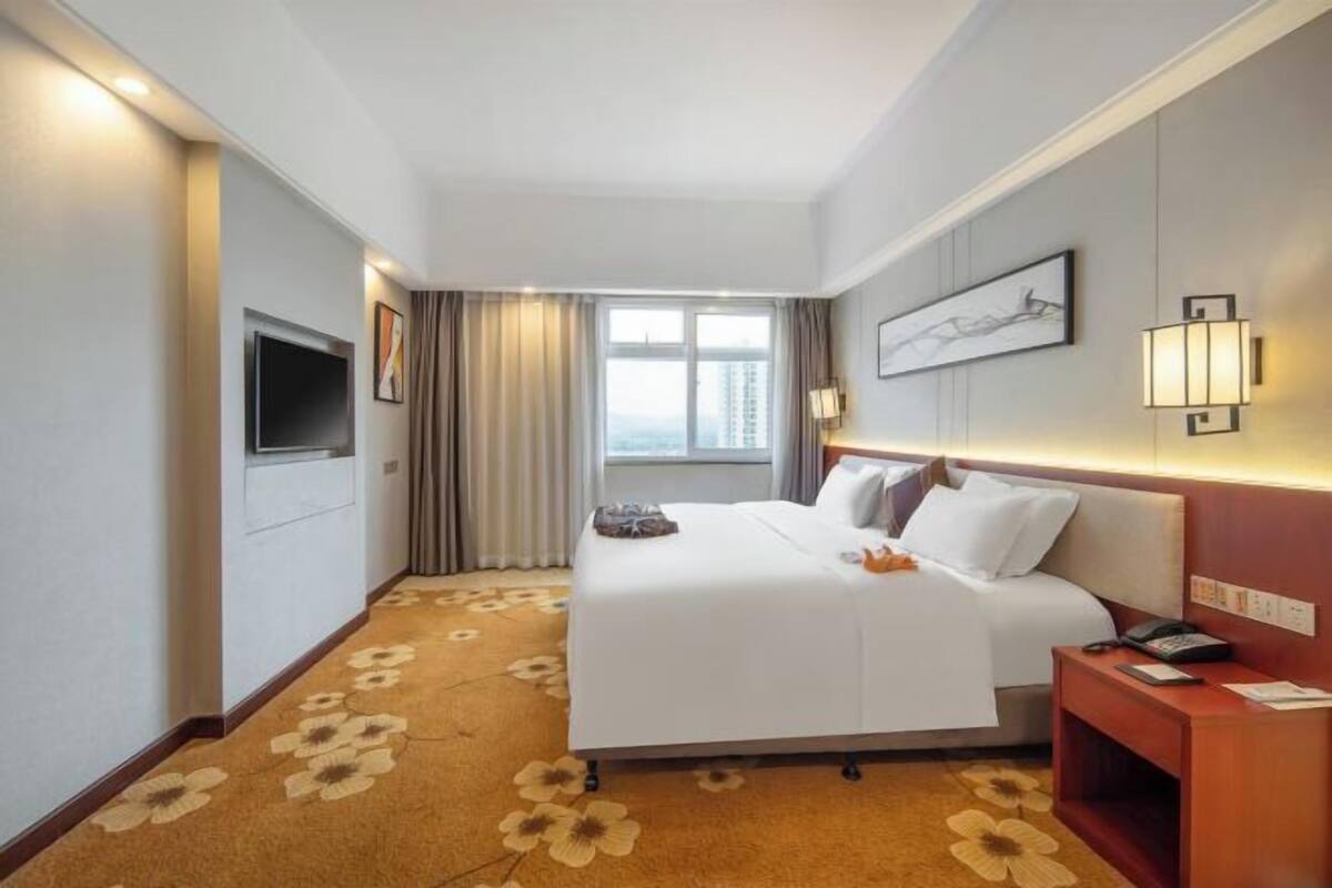 A hotel room with a large bed, a flat-screen TV, a bedside table, and a window with curtains.