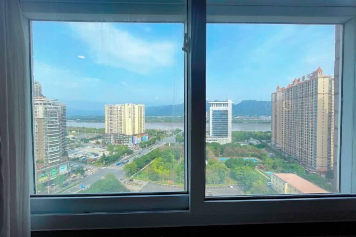 A view from a window of a high-rise building overlooking a cityscape with multiple tall buildings, a river, and greenery.