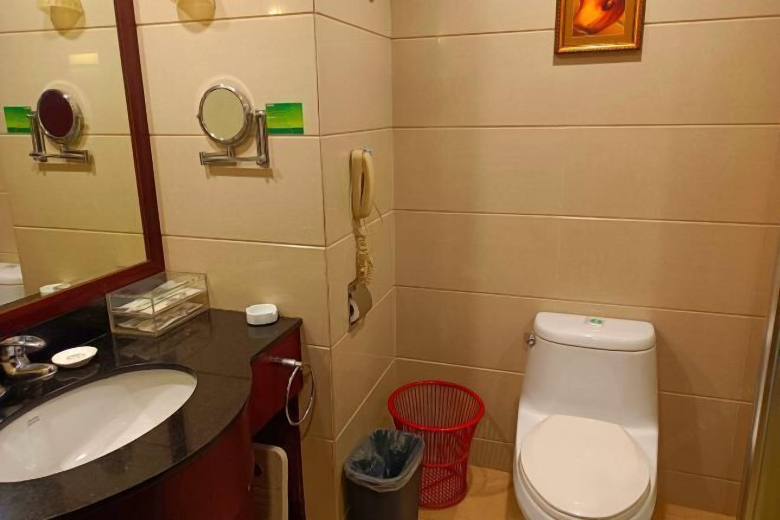 Un baño con lavabo, espejo, inodoro, cubo de basura y una cesta roja.