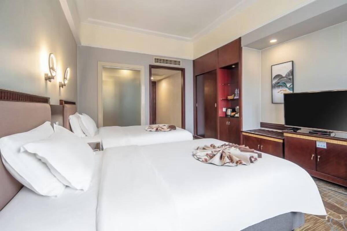 A hotel room with two beds, a television, a wardrobe, and a bathroom visible through an open door.