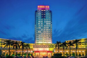 A multi-story hotel with a prominent sign at the top, a well-lit facade, and a parking lot with several cars. - Conch International Hotel (Yingde)