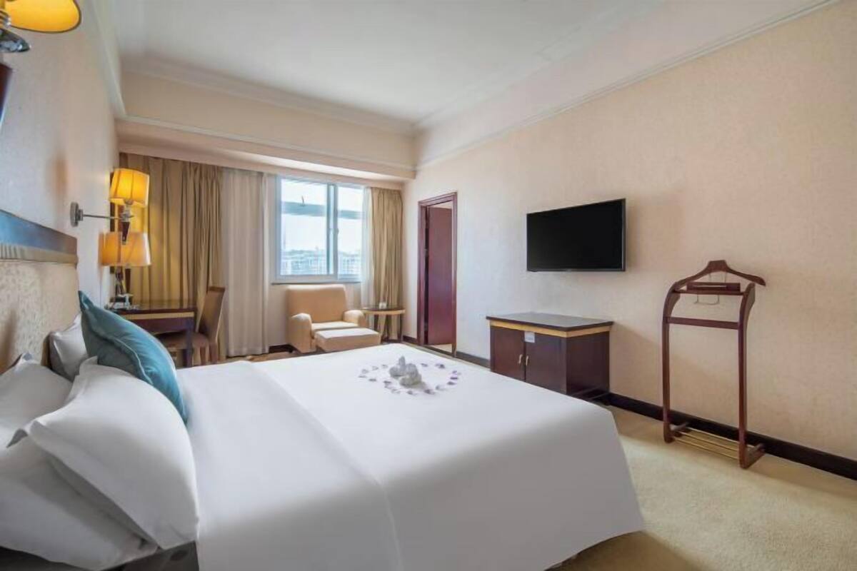 A hotel room with a bed, a desk, a chair, a TV, and a window with a view.