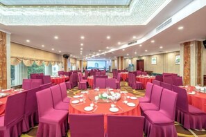 Une salle de banquet avec des tables rondes et des chaises, un plafond haut doté d’un éclairage encastré et un grand écran en arrière-plan.