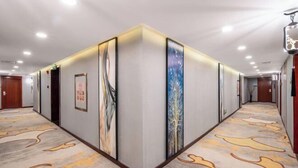 A hotel corridor with a patterned carpet, framed artwork on the walls, and doors leading to rooms. - Conch International Hotel (Yingde)