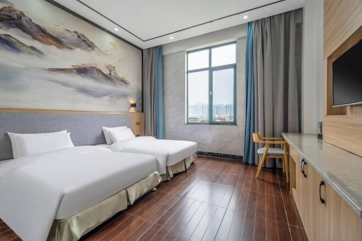 A hotel room with two beds, a large window with a city view, a TV, and a desk with a chair.