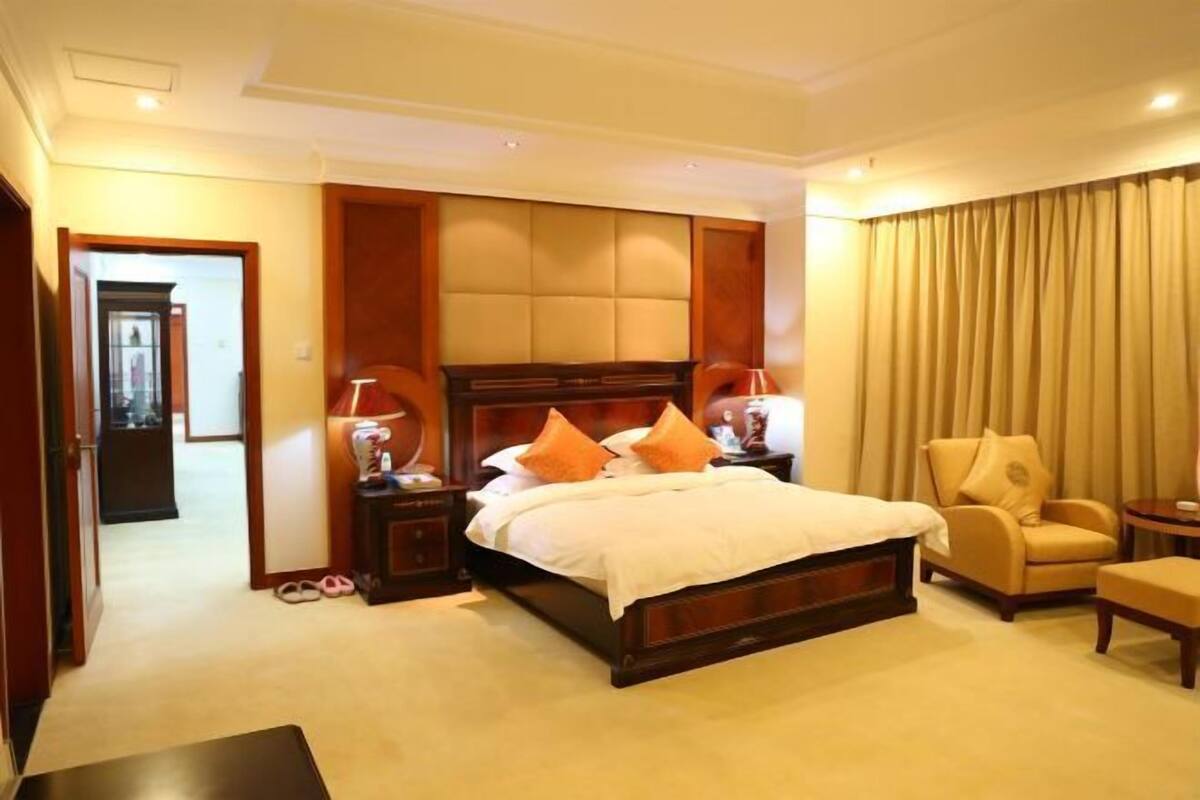 A hotel room with a large bed, a sitting area with a chair, a small table, and a nightstand with a lamp.