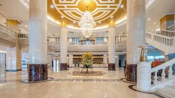 A spacious lobby with a grand chandelier, multiple floors, and a central floral arrangement.