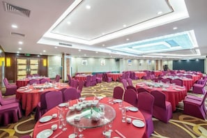 Uma sala de banquetes com mesas redondas, cadeiras e teto com iluminação embutida.