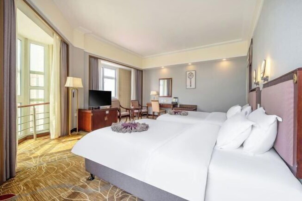 A hotel room with a large bed, a desk, a chair, a television, and a window.