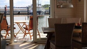 A room with a view of a dock and boats, a table with chairs, and a hanging light fixture. - Houseboat Liliput Comfortable Holiday Residence (Stralsund)