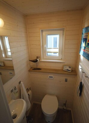 A compact wooden bathroom with a window, a sink, and a toilet.