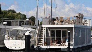 A houseboat docked at a marina with a covered outdoor seating area and a staircase leading to the upper deck. - Houseboat Liliput Comfortable Holiday Residence (Stralsund)