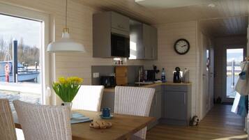 A cozy kitchen with a dining area, wooden floors, and a view of boats outside.