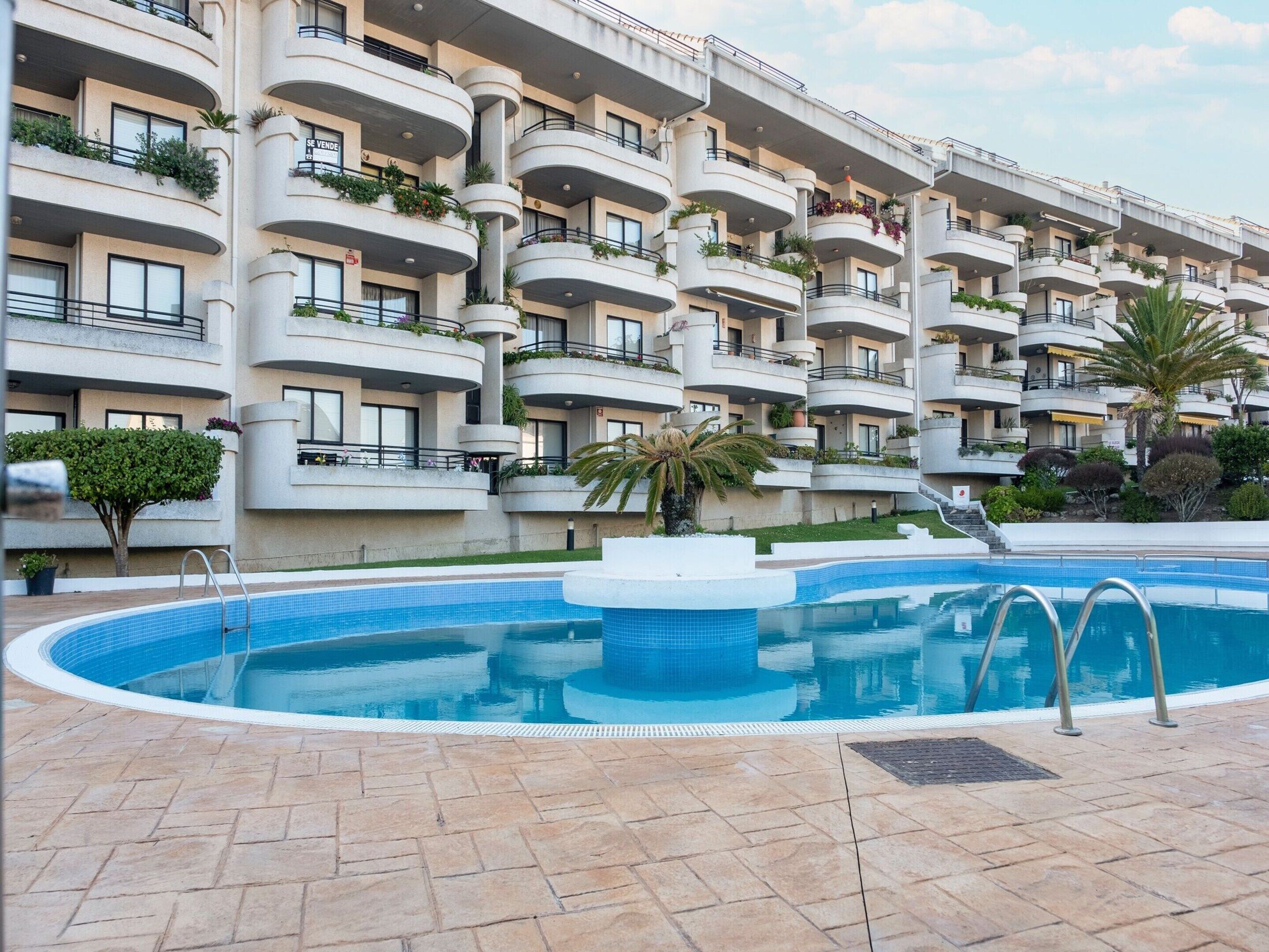 A modern hotel with a swimming pool, multiple balconies, and lush landscaping.