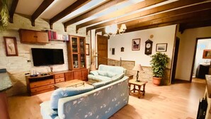 A cozy living room with a blue sofa, wooden beams, a television, and a fireplace. - Belvilla by oyo Home Holidays Casa Rural Tijoco (Adeje)