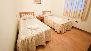 A room with two single beds, wooden headboards, a nightstand with a lamp, a framed picture on the wall, and a window with vertical blinds. - Belvilla by oyo Home Holidays Casa Rural Tijoco (Adeje)