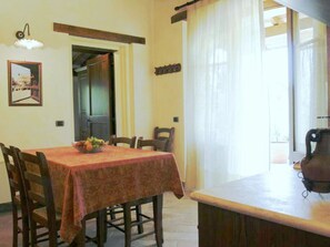 Un coin repas avec une table dressée pour quatre personnes, un panier de fruits sur la table et une vue sur l’extérieur par une fenêtre.