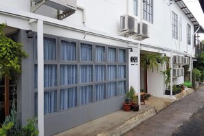 A white building with a large garage door, potted plants, and a small entrance with a door. - Oon Poshtel X Cafe (Chiang Mai)