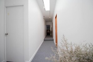A narrow hallway with white walls, a grey carpet, and a door at the end. - Oon Poshtel X Cafe (Chiang Mai)
