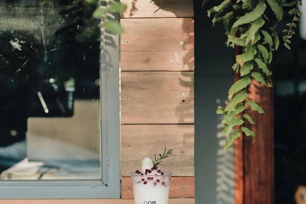 A glass of drink with berries and a sprig of rosemary on a wooden surface. - Oon Poshtel X Cafe (Chiang Mai)