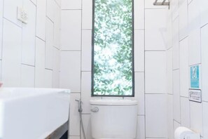 A bathroom with white tiled walls, a toilet, a window with a view of trees, and a hand dryer. - Oon Poshtel X Cafe (Chiang Mai)