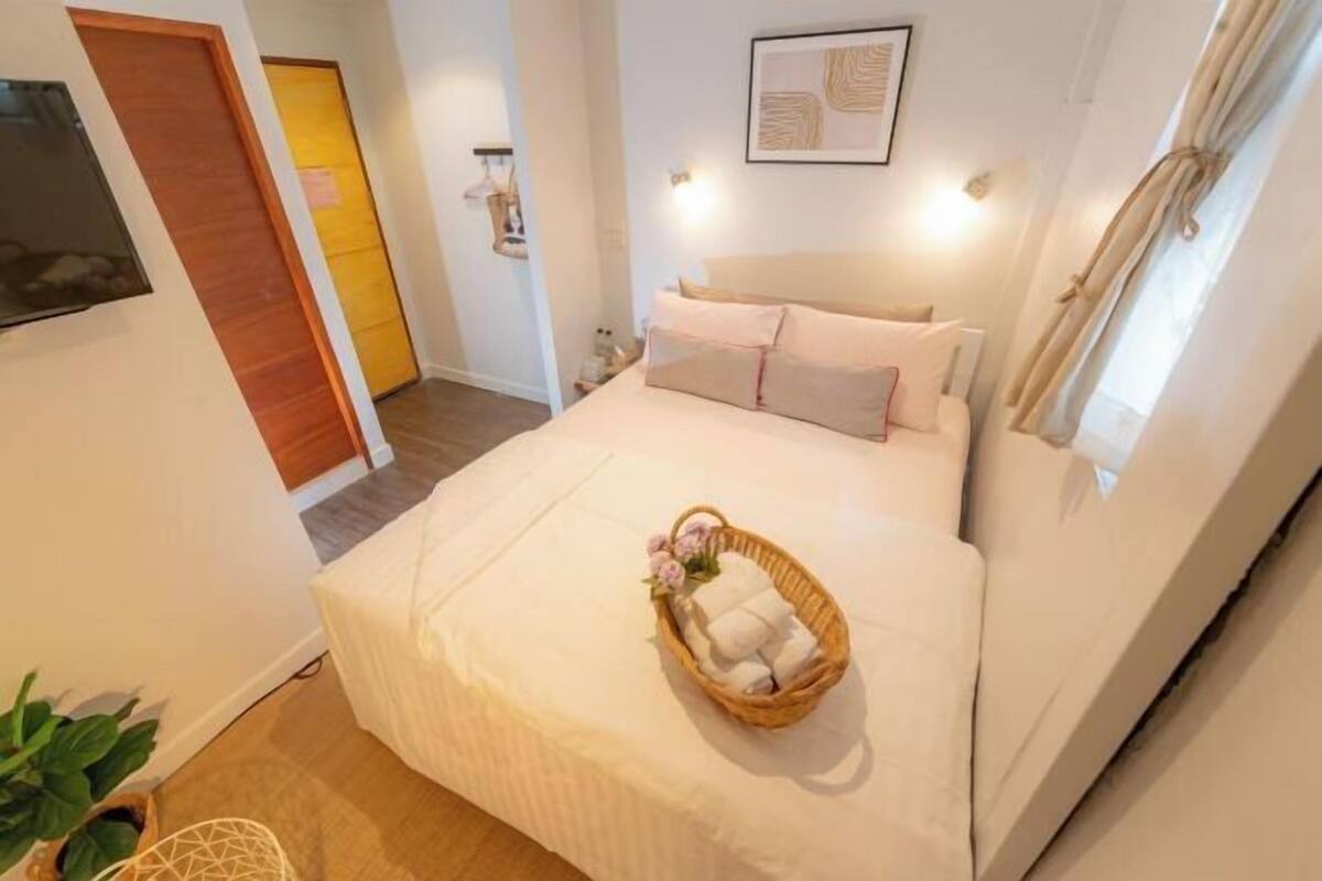 Quarto bem arrumado com cama, mesa de cabeceira, obra de arte na parede e janela com cortinas.