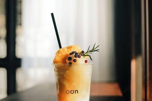 A clear glass with a straw, containing a layered beverage, garnished with a slice of orange, a sprig of rosemary, and a few berries. - Oon Poshtel X Cafe (Chiang Mai)