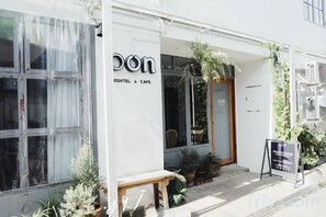 A cafe with a clear entrance, a wooden bench outside, and potted plants around. - Oon Poshtel X Cafe (Chiang Mai)